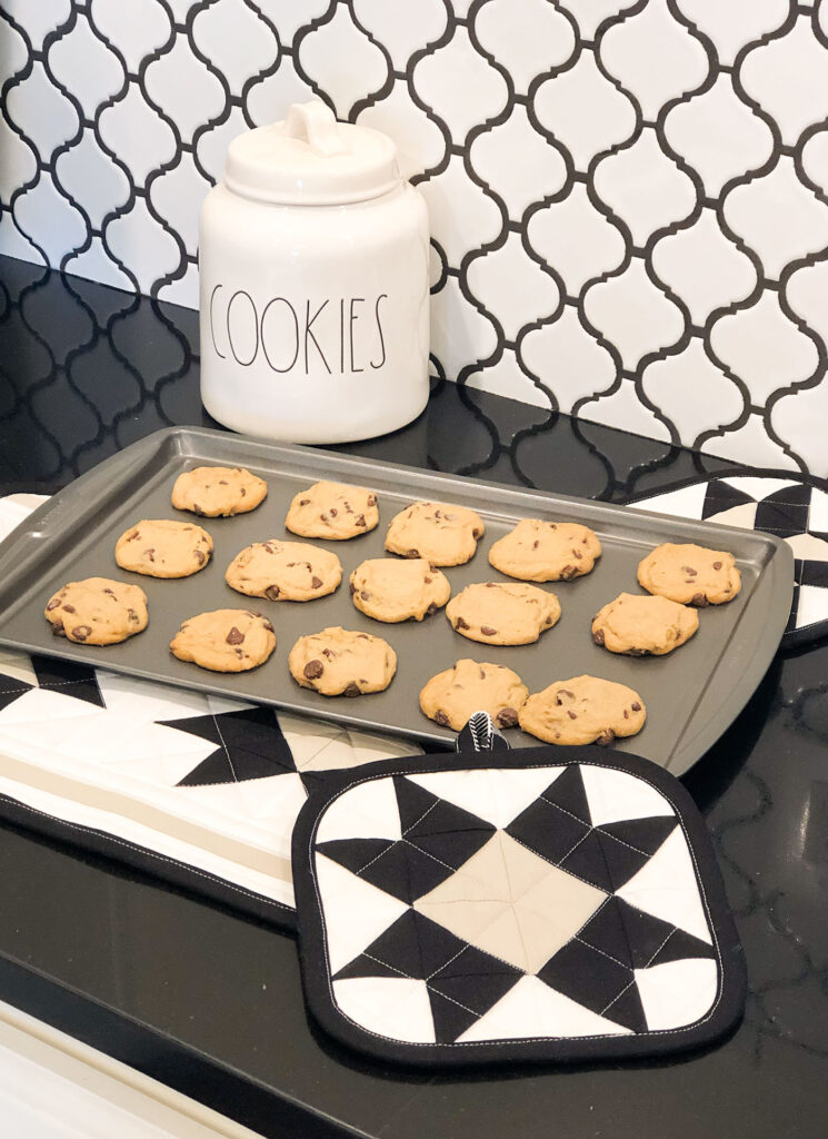 Cookies sit on a pan set on a trivet next to hot pads