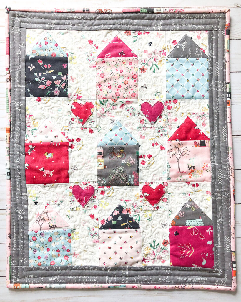 Community Love mini quilt by Top US Sewing Blog Ameroonie Designs. Image of: close up of mini quilt with houses and hearts.