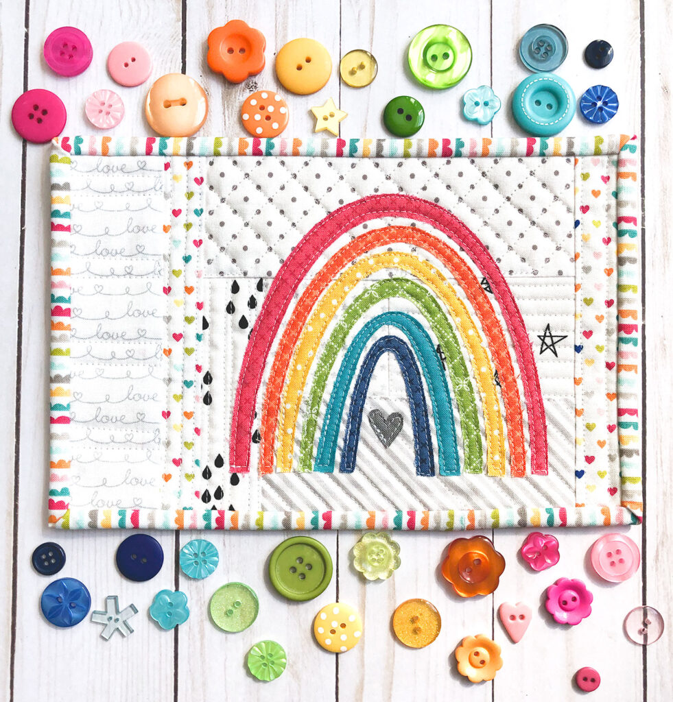 Mini Rainbow Applique Pattern by top US sewing blog Ameroonie Designs image of: mug rug with quilt as you go background and raw edge applique rainbow.