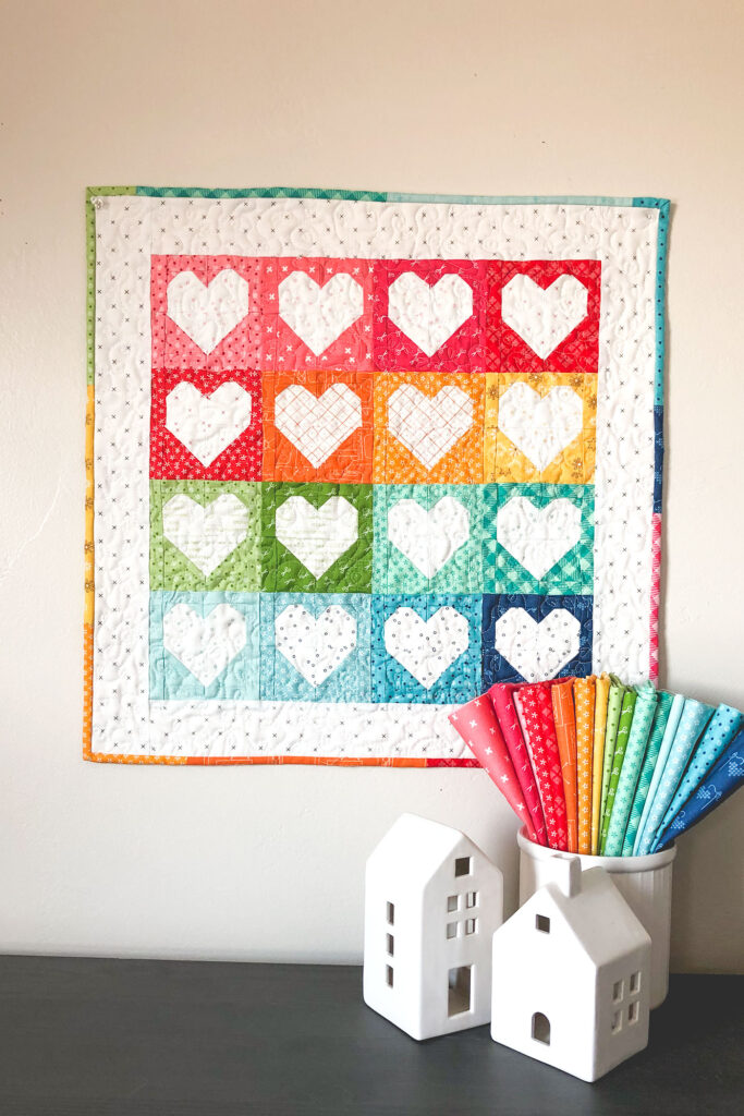 Heart Mini Quilt by top US sewing blog Ameroonie Designs. Image of:Mini quilt with rainbow hearts and fabric.