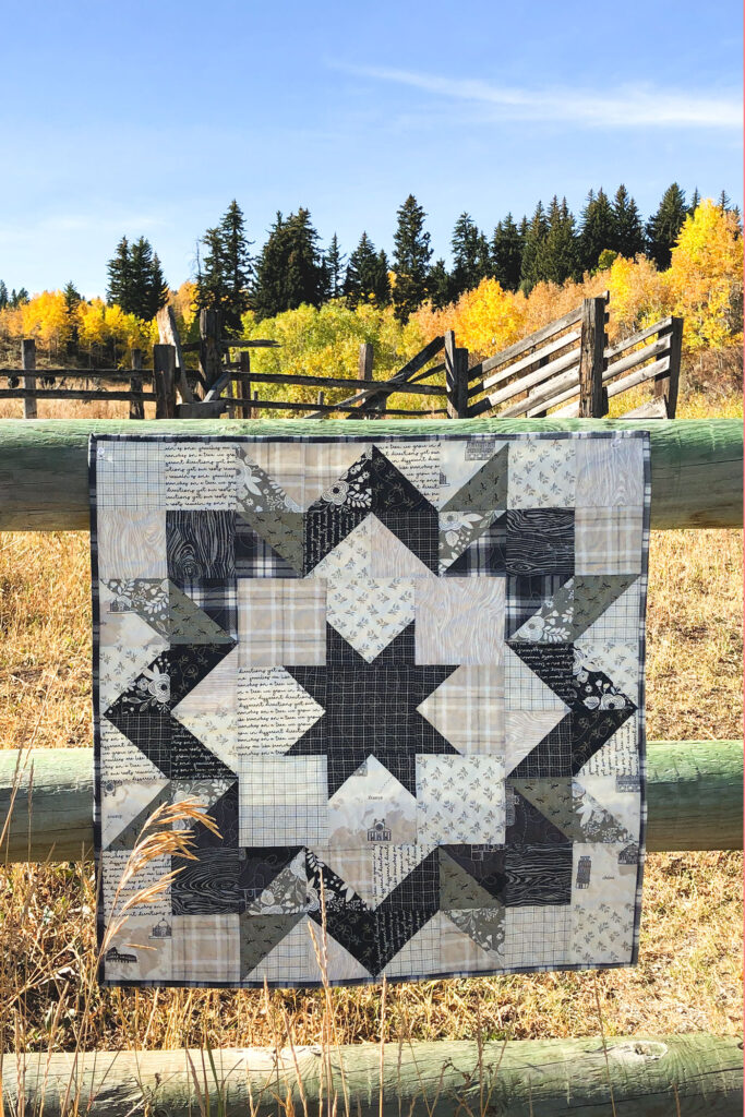 Fabric barn quilt by top US sewing blog Ameroonie Designs. Image of barn quilt on fence with autumn trees.