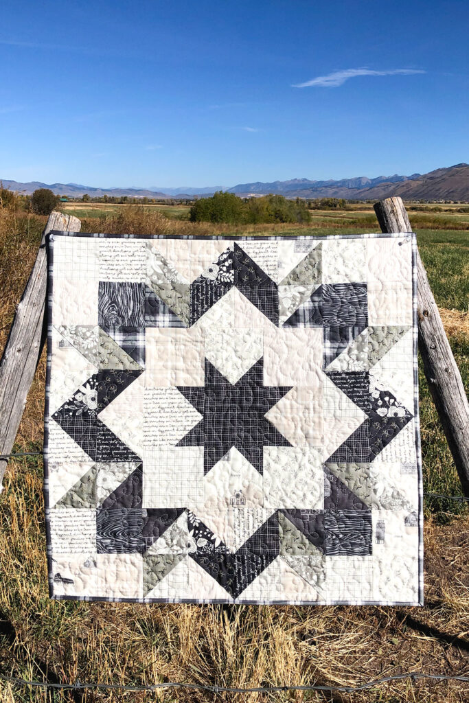 Fabric barn quilt by top US sewing blog Ameroonie Designs. Image of mini quilt with farming valley behind.