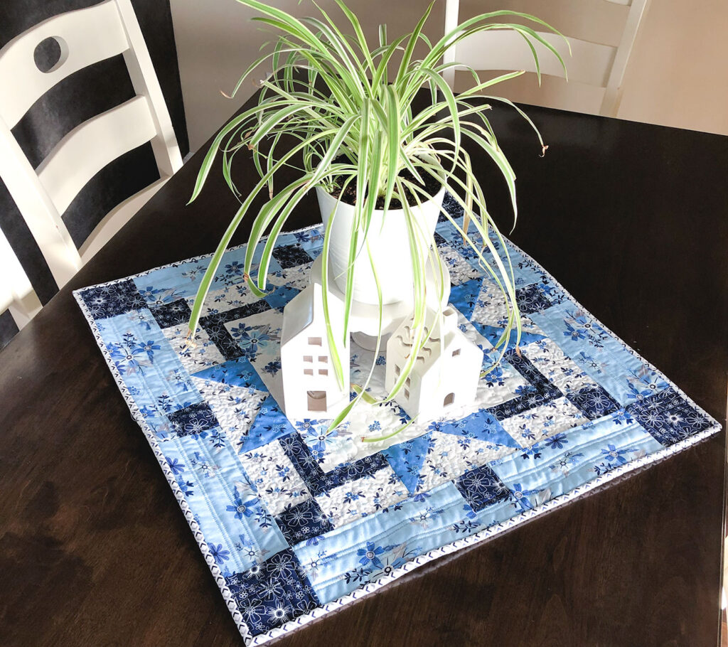 Easy table topper quilt by Top US sewing blog Ameroonie Designs. Image of: table topper with plant and houses.