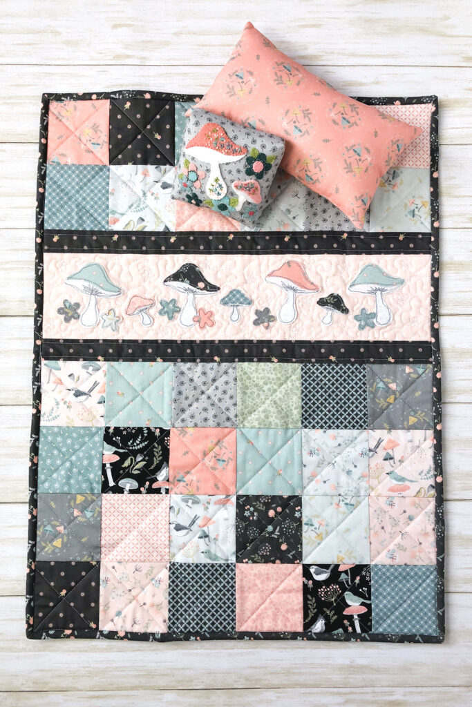 Patchwork doll quilt by top US sewing blog Ameroonie Designs. Image of doll quilt with applique strip and pillows.