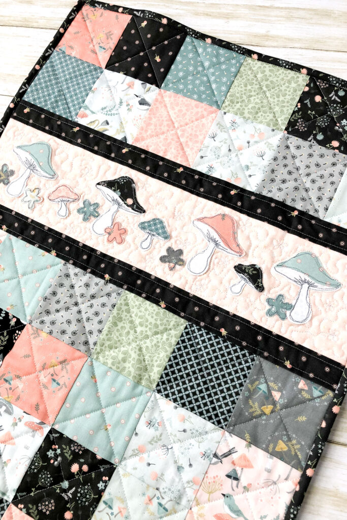 Patchwork doll quilt by top US sewing blog Ameroonie Designs. Image of close up of applique on patchwork doll quilt.