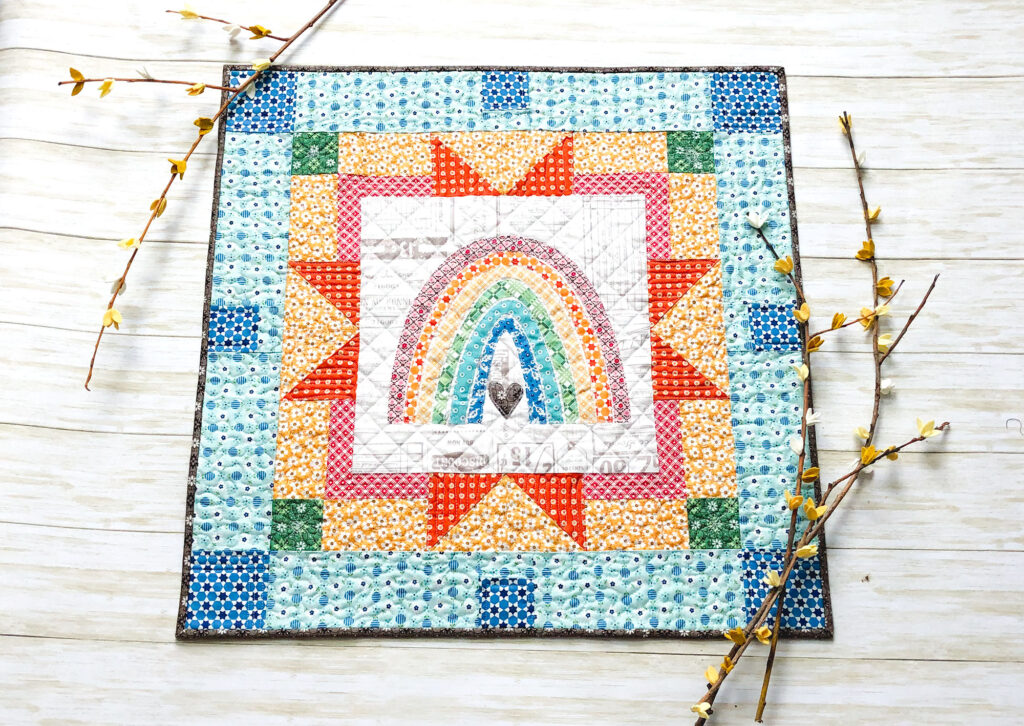 Delightful rainbow mini quilt by top US sewing blog Ameroonie Designs. Image of: rainbow mini quilt with flowered branches.