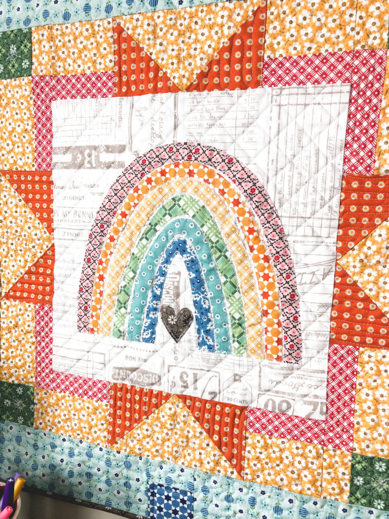 Delightful rainbow mini quilt by top US sewing blog Ameroonie Designs. Image of rainbow applique on mini quilt.