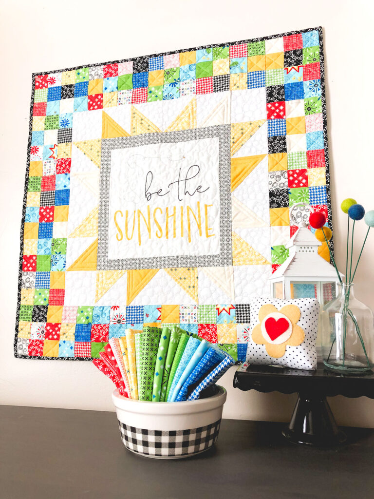 Sew a stunning mini quilt with a fabric panel by top US sewing blog Ameroonie Designs. Image of mini quilt with fabric and decorations.