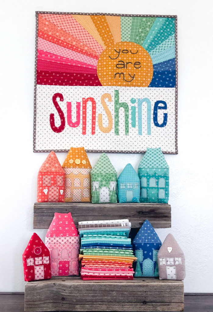 Rainbow Sunshine mini quilt sew along with top US sewing blog Ameroonie Designs. Image of mini quilt and houses with fabric.