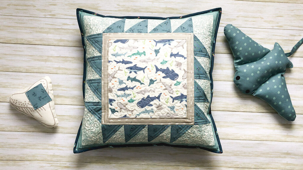 Shark teeth pillow by top US sewing blog Ameroonie Designs. Image of quilted pillow with shark stuffed animal.