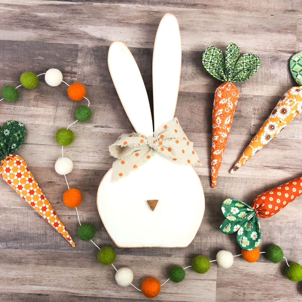 How to sew fabric carrots with top US sewing blog Ameroonie Designs. Image of wooden bunny with fabric carrots and felt pom garland.