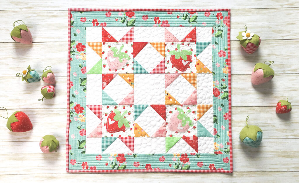 Strawberry Springtime mini quilt free pattern by top US sewing blog Ameroonie Designs. Image of mini quilt with strawberry applique and stuffed fabric strawberries.