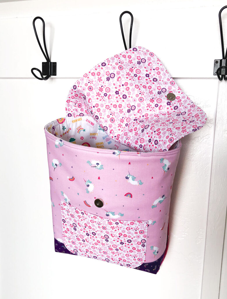 Sew an adorable backpack by top US sewing blog Ameroonie Designs. Image of pink unicorn backpack hanging from hook.