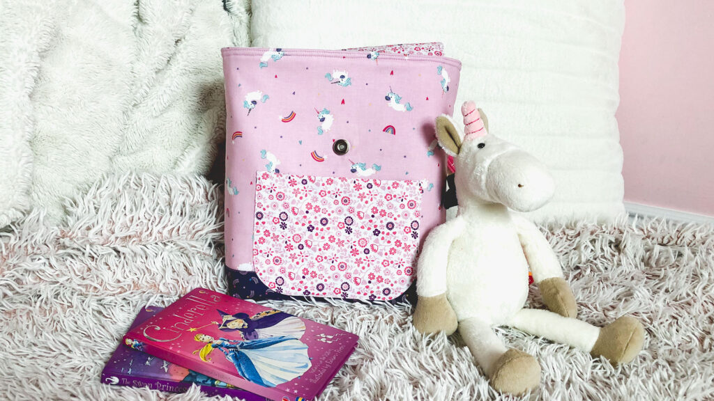 Sew an adorable backpack by top US sewing blog Ameroonie Designs. Image of pink backpack with stuffed unicorn, pillow and books.