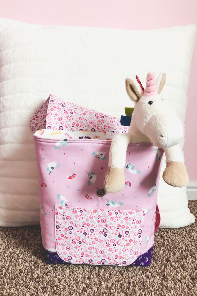 Sew an adorable backpack by top US sewing blog Ameroonie Designs. Image of stuffed unicorn hanging out of pink backpack.