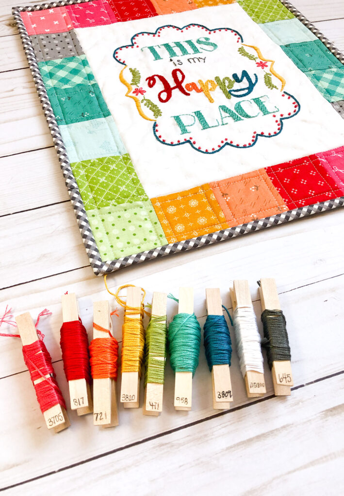 Turn your embroidery into a stunning mini quilt by Top US sewing blog Ameroonie Designs. Image of mini quilt and clothes pins with embroidery floss to show floss colors.