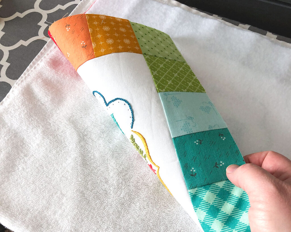 Turn your embroidery into a stunning mini quilt by Top US sewing blog Ameroonie Designs. Image of embroidery face down on towel for pressing to prevent distortion of stitches.