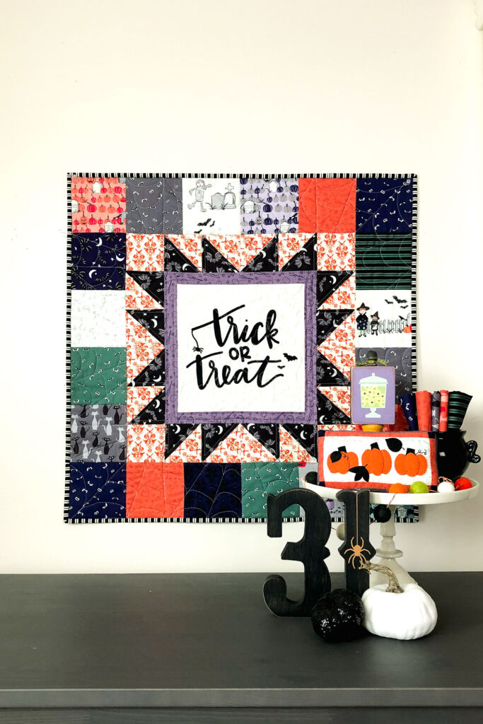 Turn a fabric panel into a stunning mini quilt from Top US sewing blog Ameroonie Designs. Image of mini quilt with Halloween decorations including mini appliqued pillow.