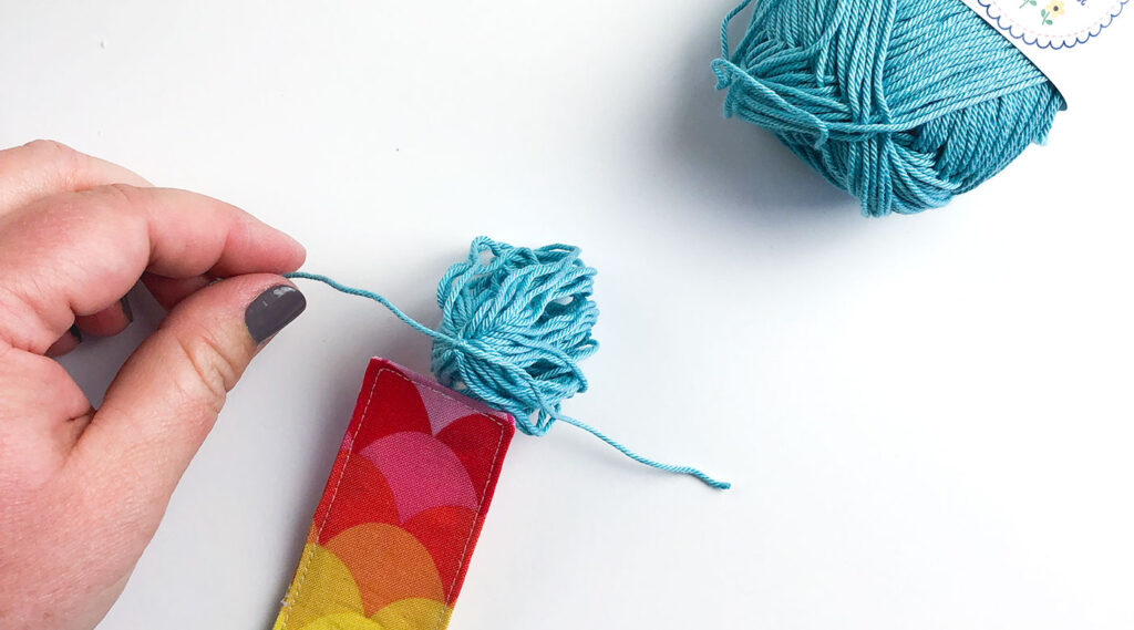 How to sew a tasseled fabric bookmark with top US sewing blog Ameroonie Designs. Image of tying knot at top of tassel and securing it to bookmark.