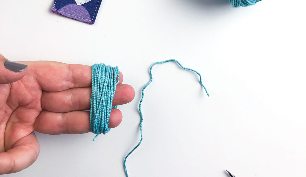 How to sew a tasseled fabric bookmark with top US sewing blog Ameroonie Designs. Image of yarn wrapped around three fingers to begin making tassel.