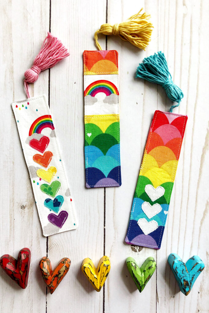 How to sew a tasseled fabric bookmark with top US sewing blog Ameroonie Designs. Image of three rainbow colored fabric bookmarks.