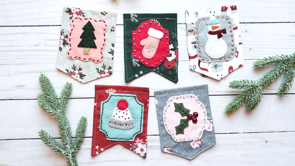 Gorgeous winter mini banner sneak peek with top US sewing blog Ameroonie Designs. Image of mini flags with wool felt applique in winter themes.