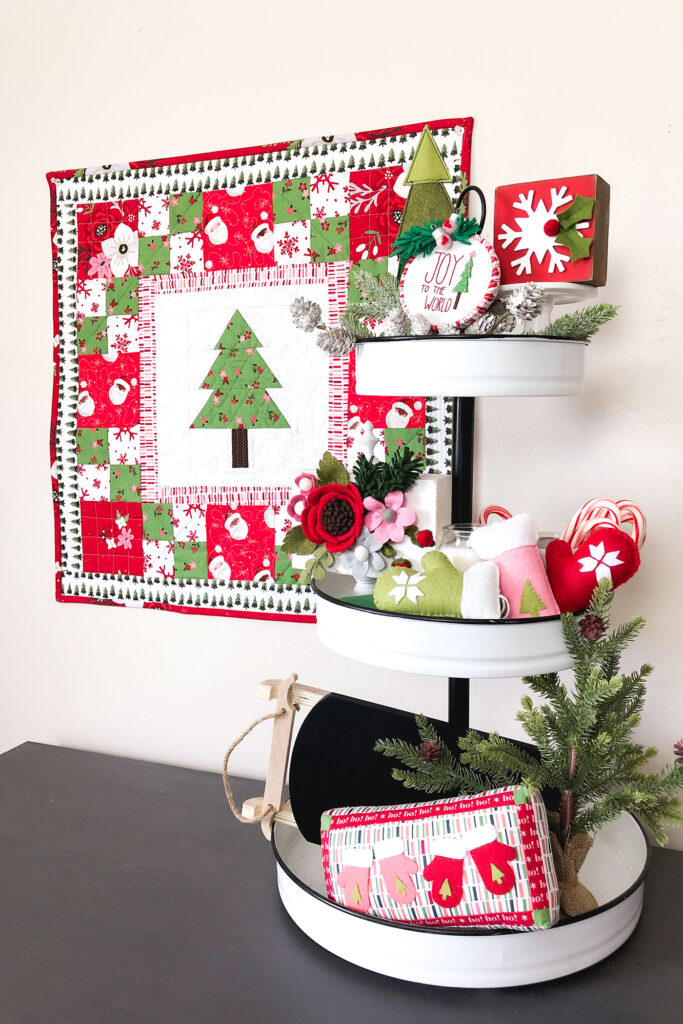 How to sew a delightful holiday mini quilt by top US sewing blog Ameroonie Designs. Image of tiered tray with felt mittens, mini pillow and greenery.