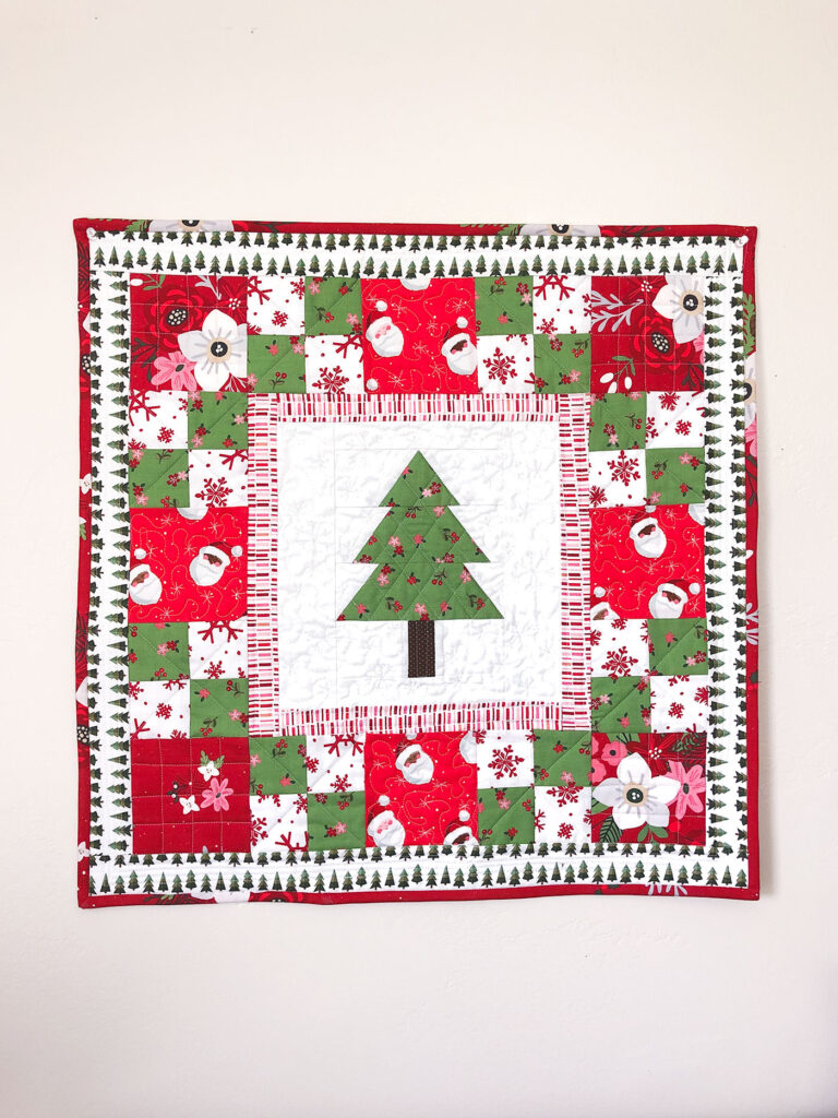 How to sew a delightful holiday mini quilt by top US sewing blog Ameroonie Designs. Image of mini quilt with pieced tree center block and red and green patchwork borders.