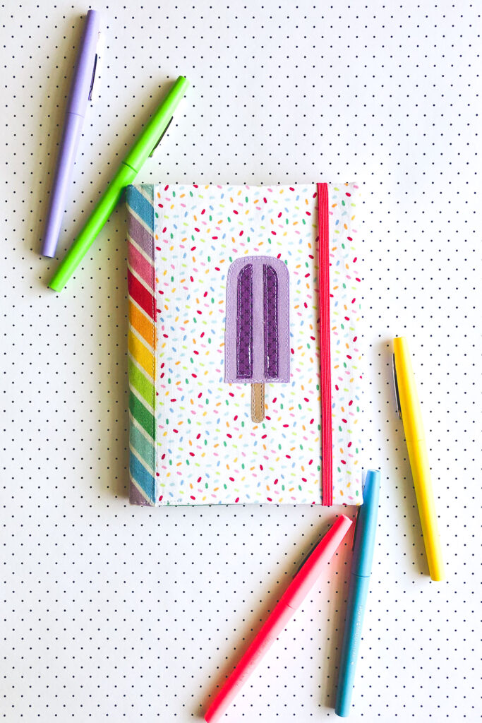 How to sew a fabric cover for a mini notebook with top US sewing blog Ameroonie Designs. Image of fabric notebook cover with popsicle applique.