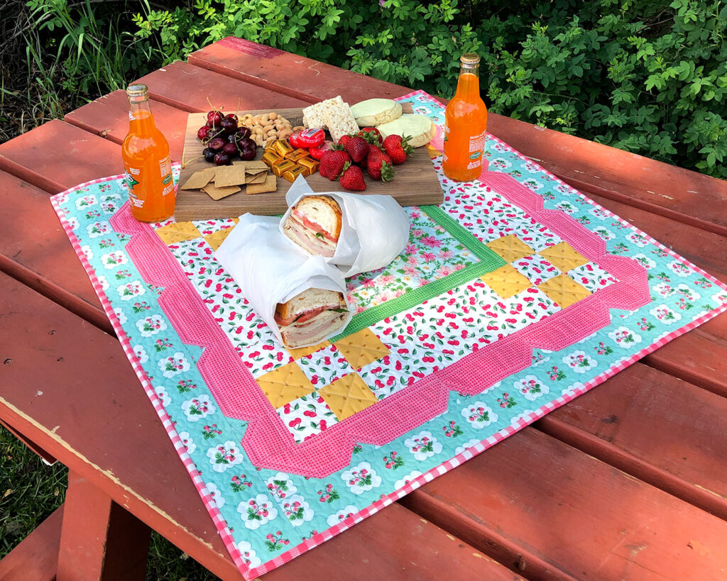 Stunning Scalloped Table Topper by top US sewing blog Ameroonie Designs. Image of table topper on picnic table with charcuterie board and sandwiches.