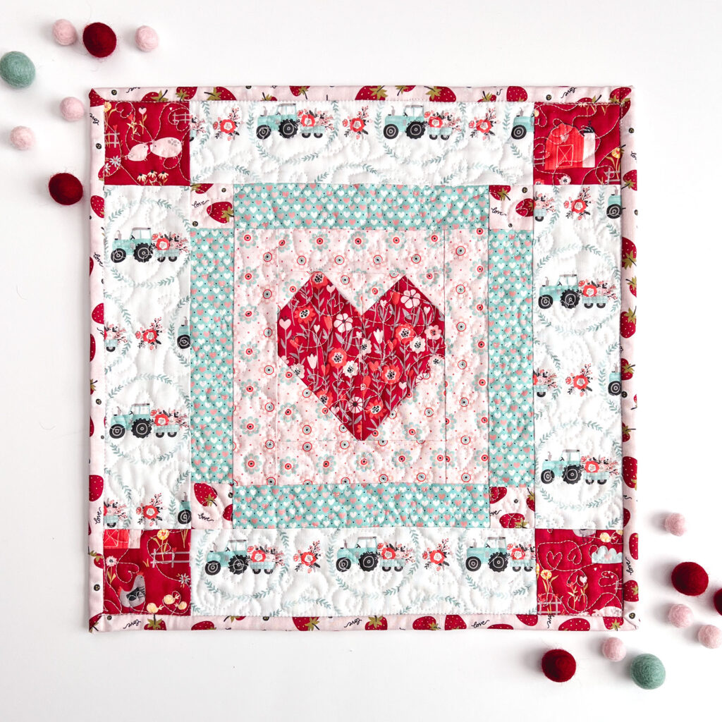 Valentine's Day decorations with top US sewing blog Ameroonie Designs. Image of mini quilt with heart and borders and felt poms as decor.