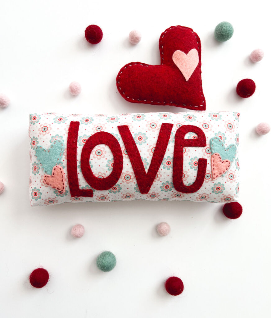 Valentine's Day decorations with top US sewing blog Ameroonie Designs. Image of mini pillow with Love appliqued on in felt. And a felt heart stuffed and stitched.
