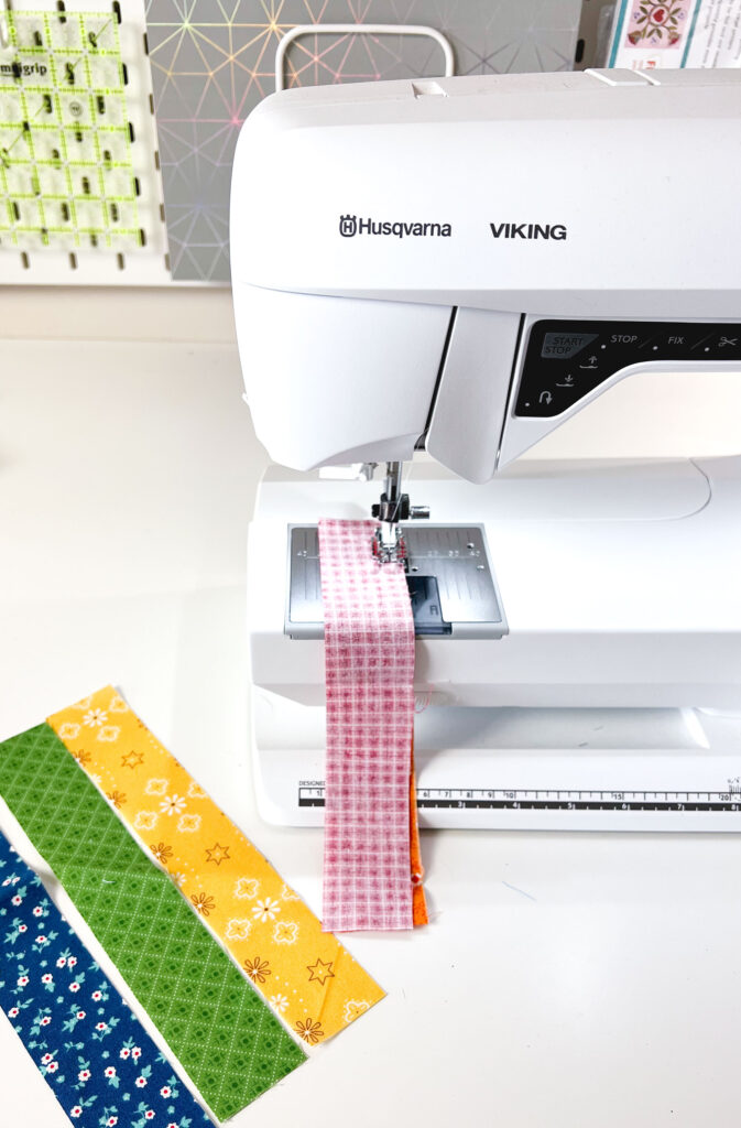 Free Needle Book Pattern from Top US sewing blog Ameroonie Designs. Image of sewing machine piecing strips of fabric together.