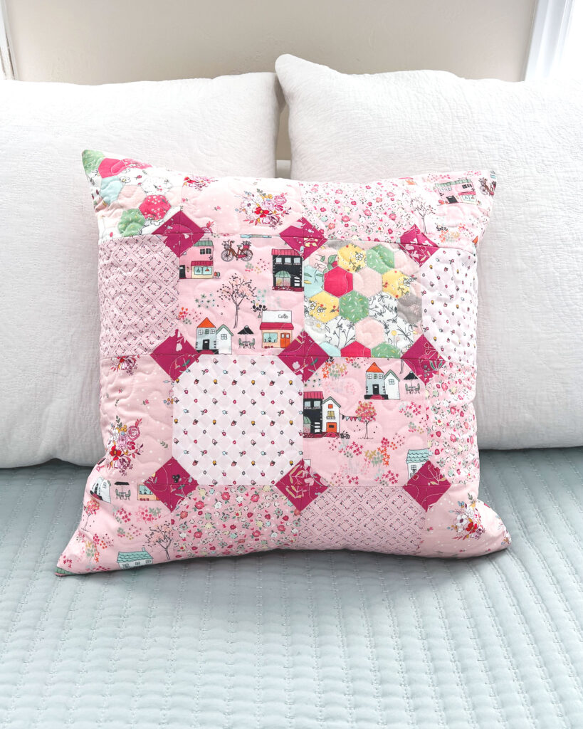 Sew a pretty patchwork pillow with pizzazz with top US sewing blog Ameroonie Designs. Image of patchwork pillow on bed.