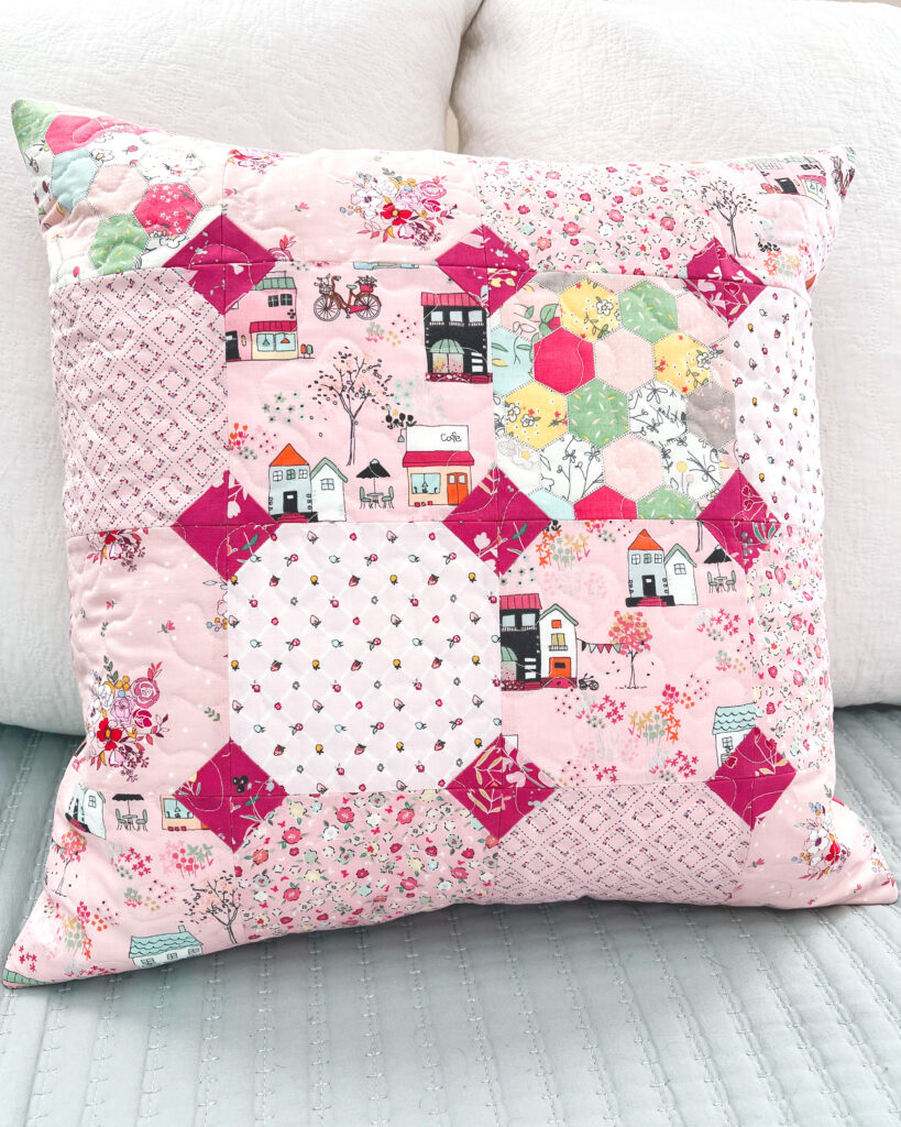 Sew a pretty patchwork pillow with pizzazz with top US sewing blog Ameroonie Designs. Image of pillow on bed.